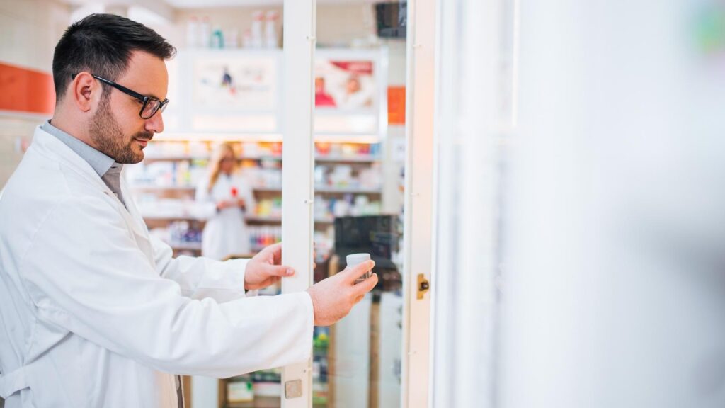 male pharmacist filling prescription and selects medicine from the shelf